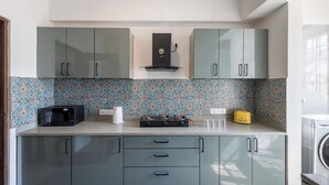 A kitchen with grey cabinets, a microwave, a gas stove, and a yellow toaster. - Emerald Apartments by Red Olive (Bengaluru)
