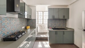 A kitchen with a gas stove, a built-in oven, a microwave, and a sink. There is a window with a view of the outside. - Emerald Apartments by Red Olive (Bengaluru)