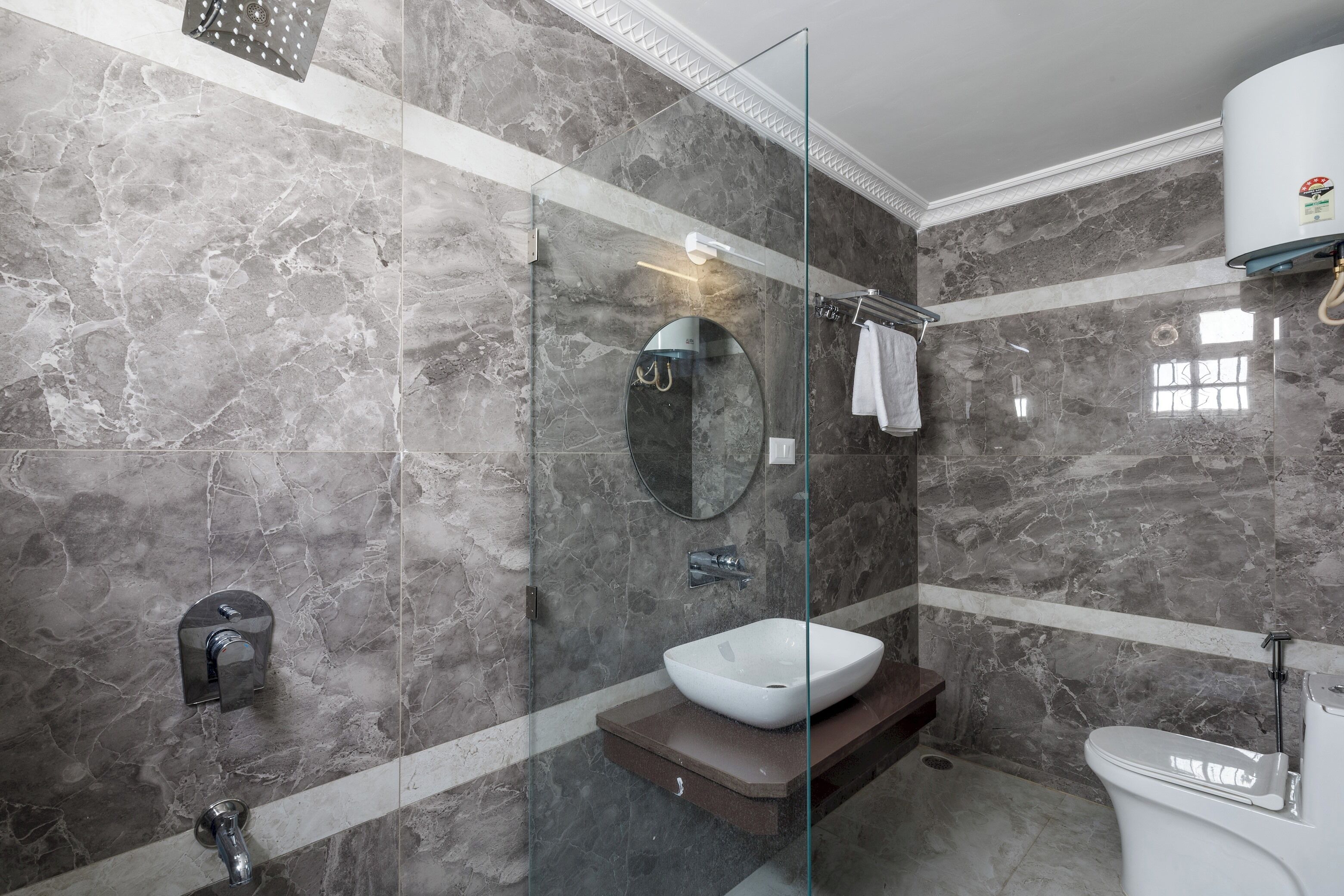 A modern bathroom with a glass-enclosed shower, a white sink, and a marble-tiled wall.