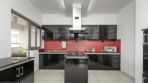 A modern kitchen with black cabinets, a central island, a microwave, and a red backsplash. - Lakeside Living by Red Olive Nr Airport 3bhk (Bengaluru)