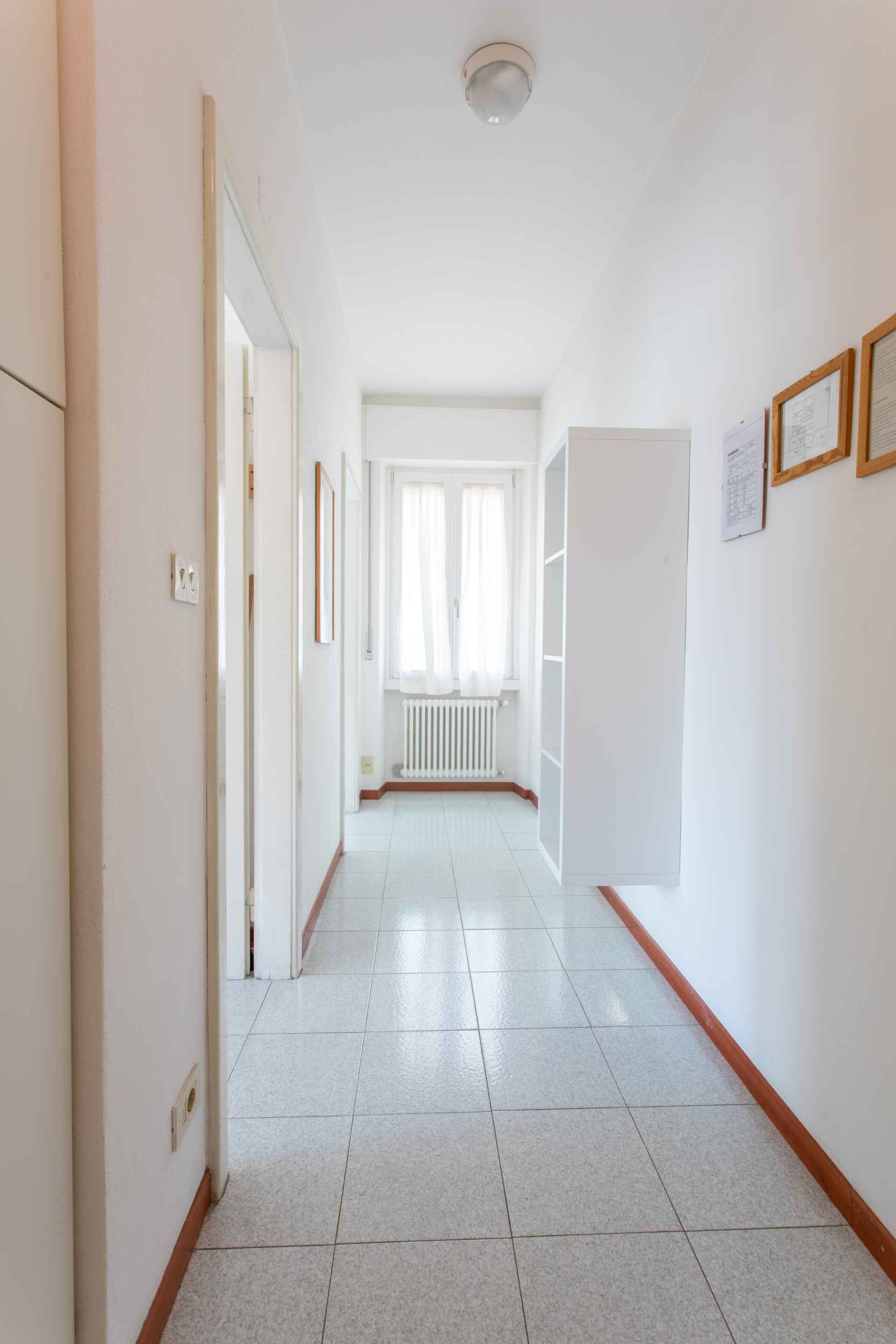 Un couloir aux murs blancs, doté d’un sol carrelé et d’un radiateur à l’arrière-plan.