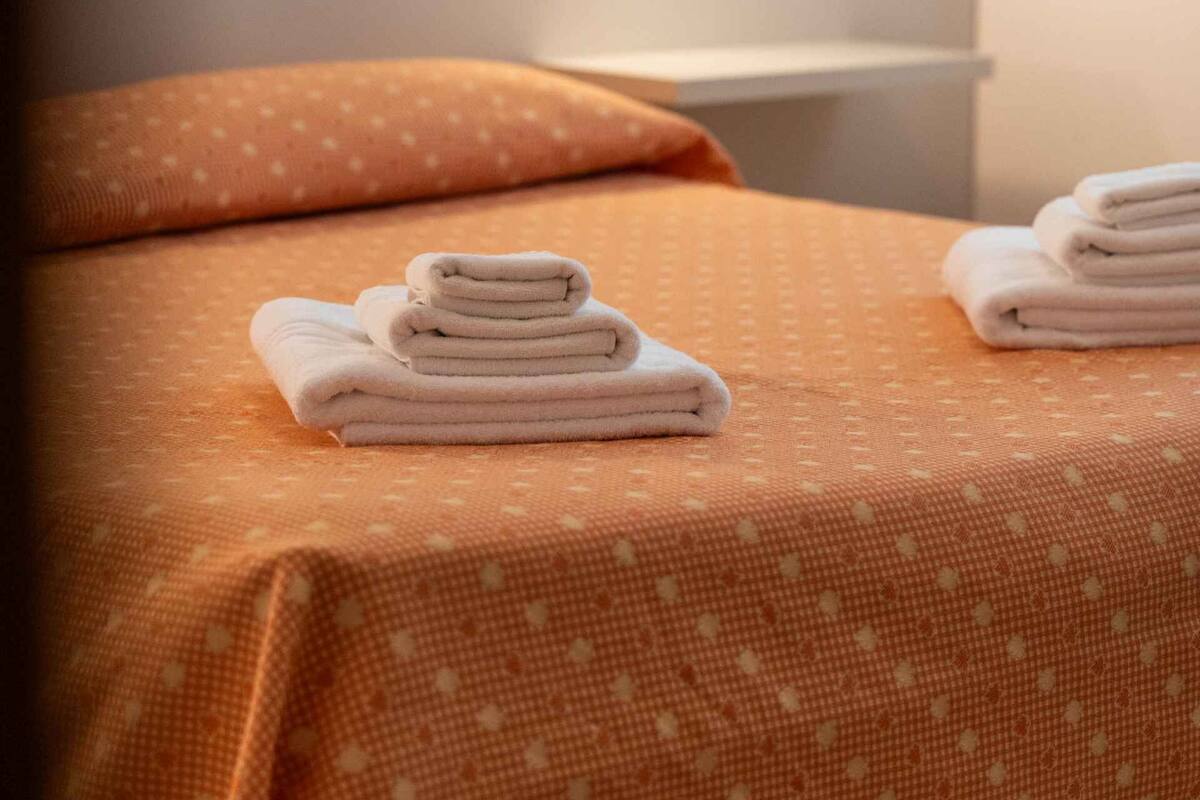 Uma cama bem arrumada com um cobre-cama estampado e duas toalhas dobradas ao lado.