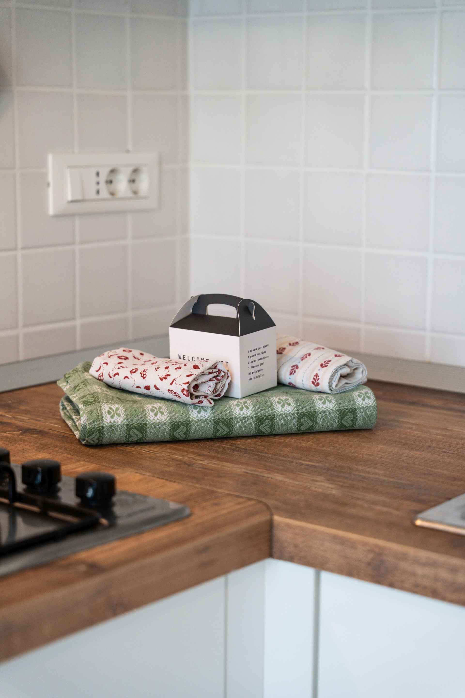 Una encimera de cocina con una toalla enrollada, una caja y un paño verde estampado.