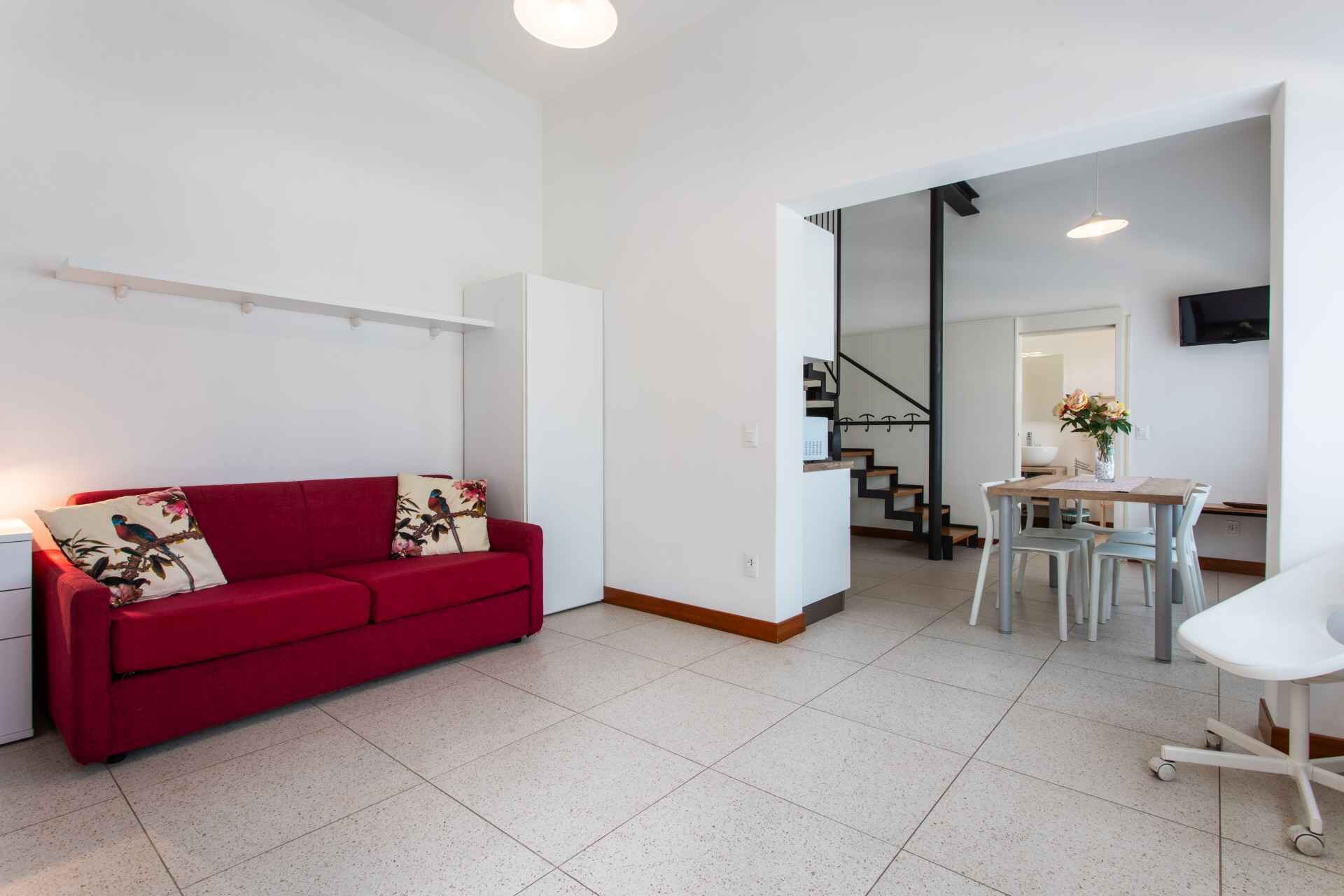 Una sala de estar moderna con un sofá rojo y un comedor con mesa y sillas.
