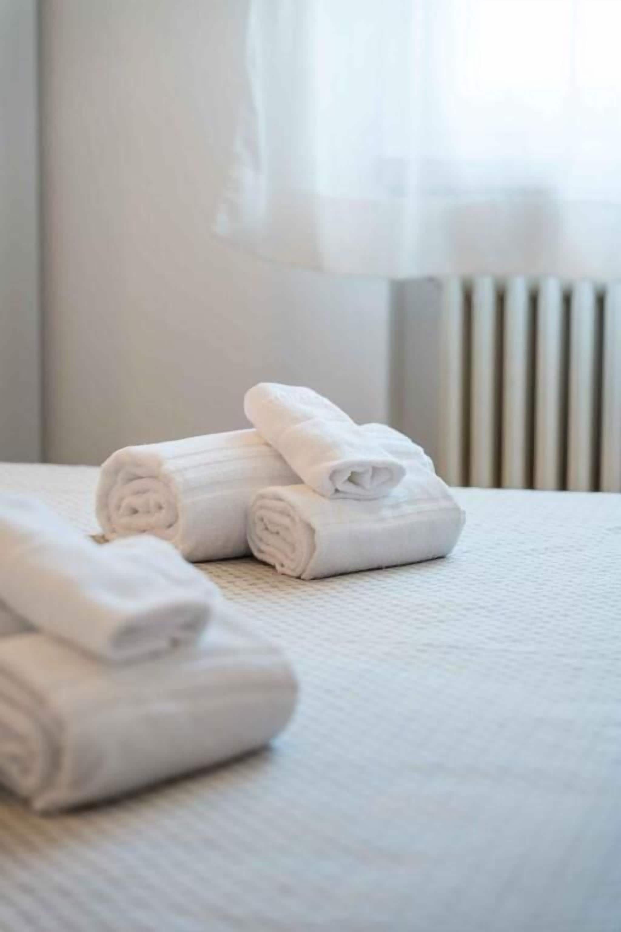 Ein ordentlich bezogenes Bett mit aufgerollten weißen Handtüchern und einem Heizkörper im Hintergrund.