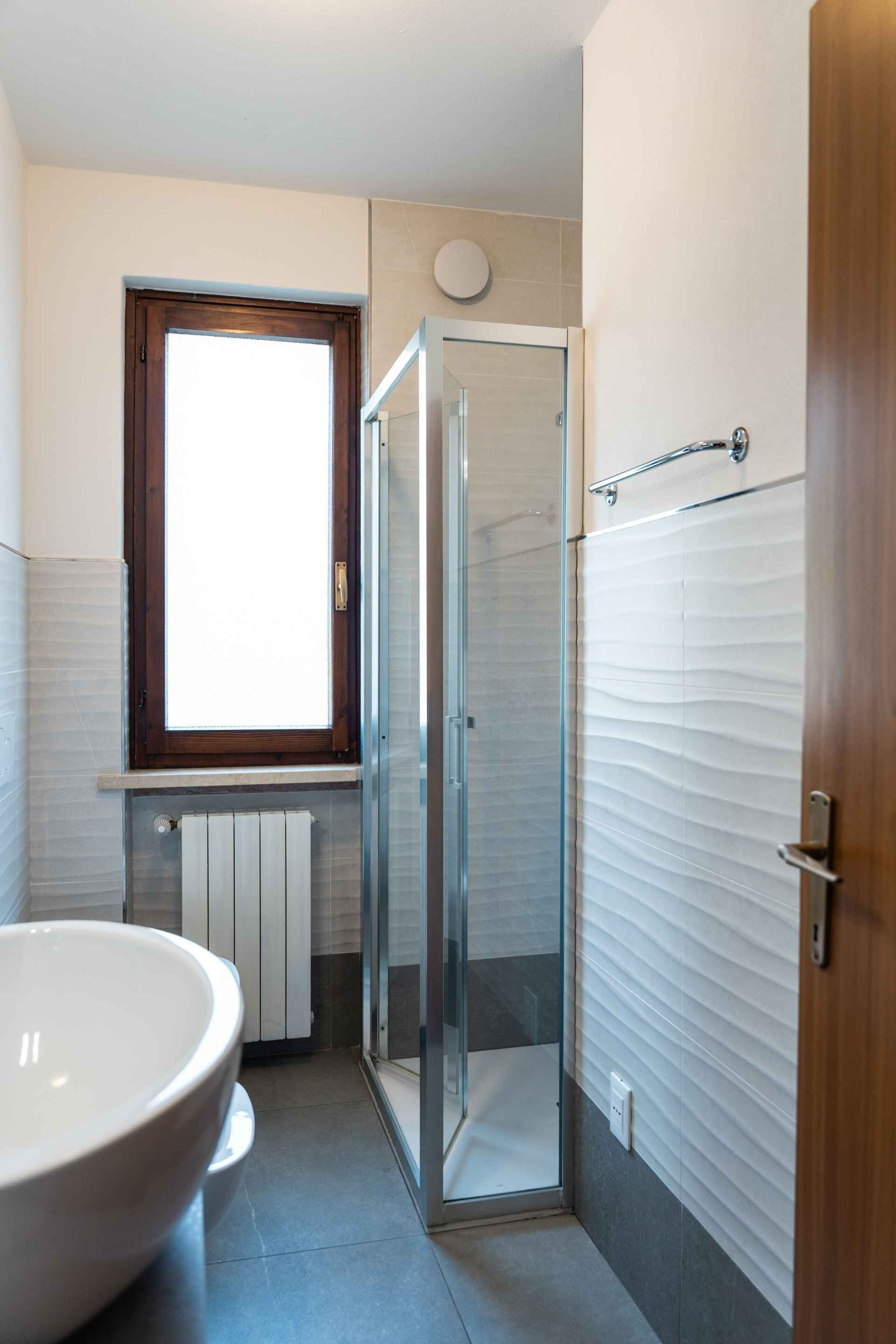 Un baño con cabina de ducha de vidrio, un lavabo grande de color blanco y una ventana sobre el lavabo.