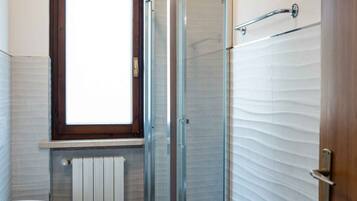 Un baño con cabina de ducha de vidrio, un lavabo grande de color blanco y una ventana sobre el lavabo.