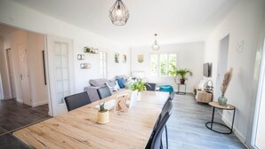 A modern living room with a wooden dining table, a sofa, and a TV. There are plants and artwork on the walls. - Villa CosyFamily-Pool-15MinPlage-Wifi-Family (Pérols)