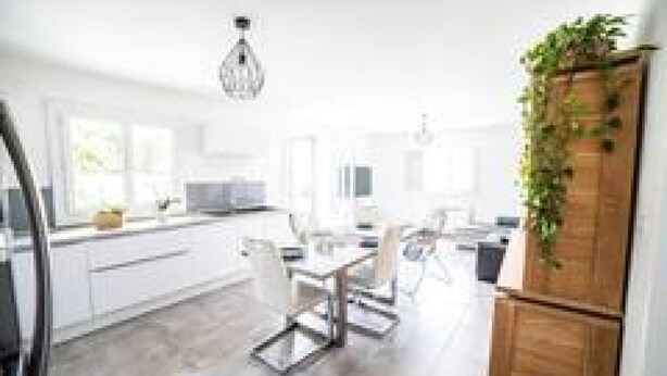 A modern kitchen with white cabinetry, a dining area with a table and chairs, and a hanging plant. - Villa CosyFamily-Pool-15MinPlage-Wifi-Family (Pérols)
