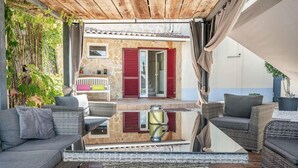 Et overdækket udendørs siddeområde med fletmøbler og et glasbord.