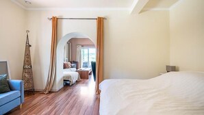 Et hotelværelse med en stor seng, en sofa og et lille bord. Der er et gardin og en taske hængende.