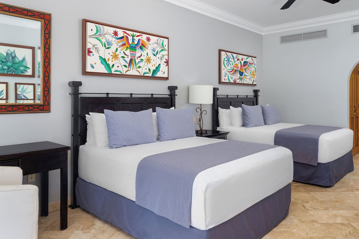 A hotel room with two beds, a desk, and artwork on the walls.