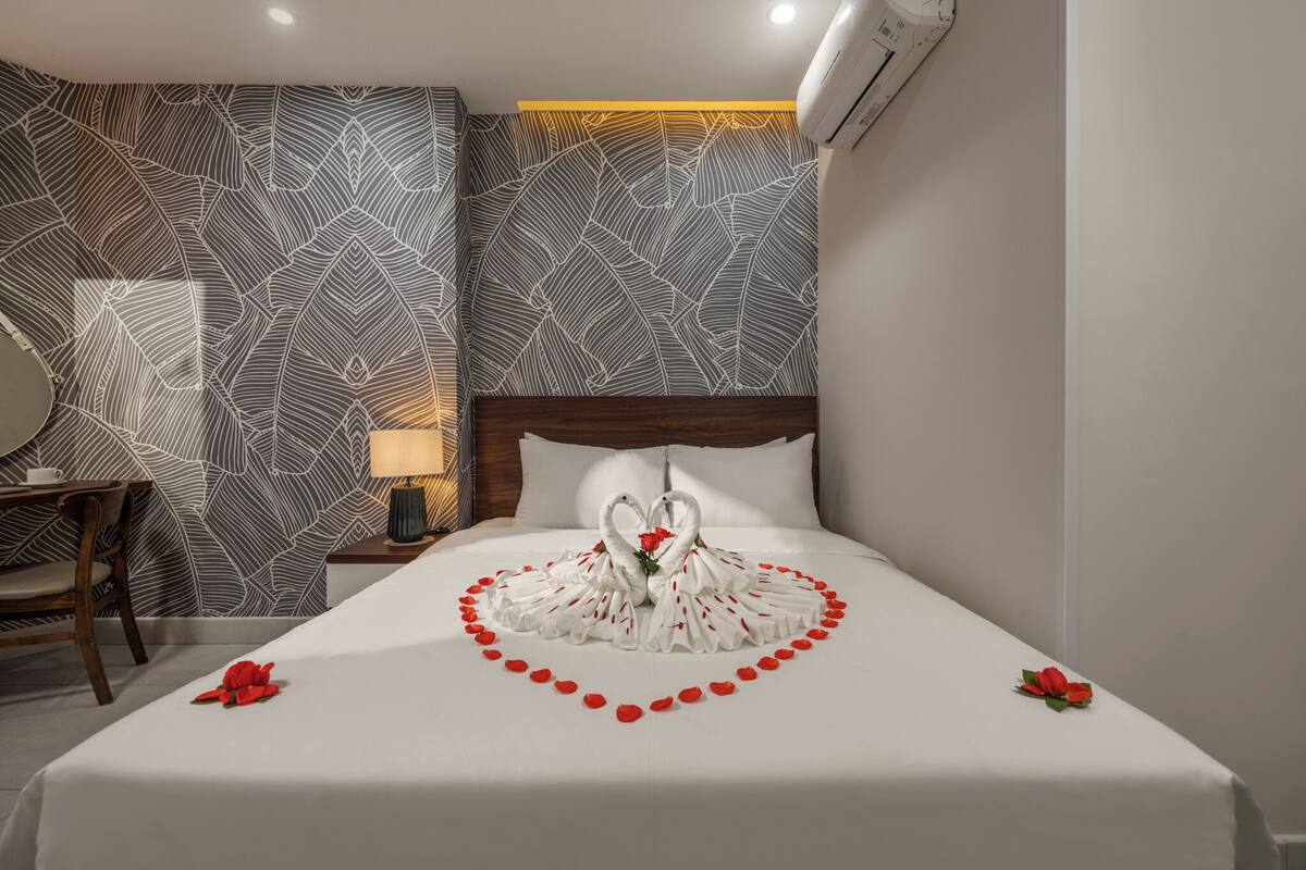 A hotel room with a bed featuring a heart-shaped towel arrangement and red rose decorations.