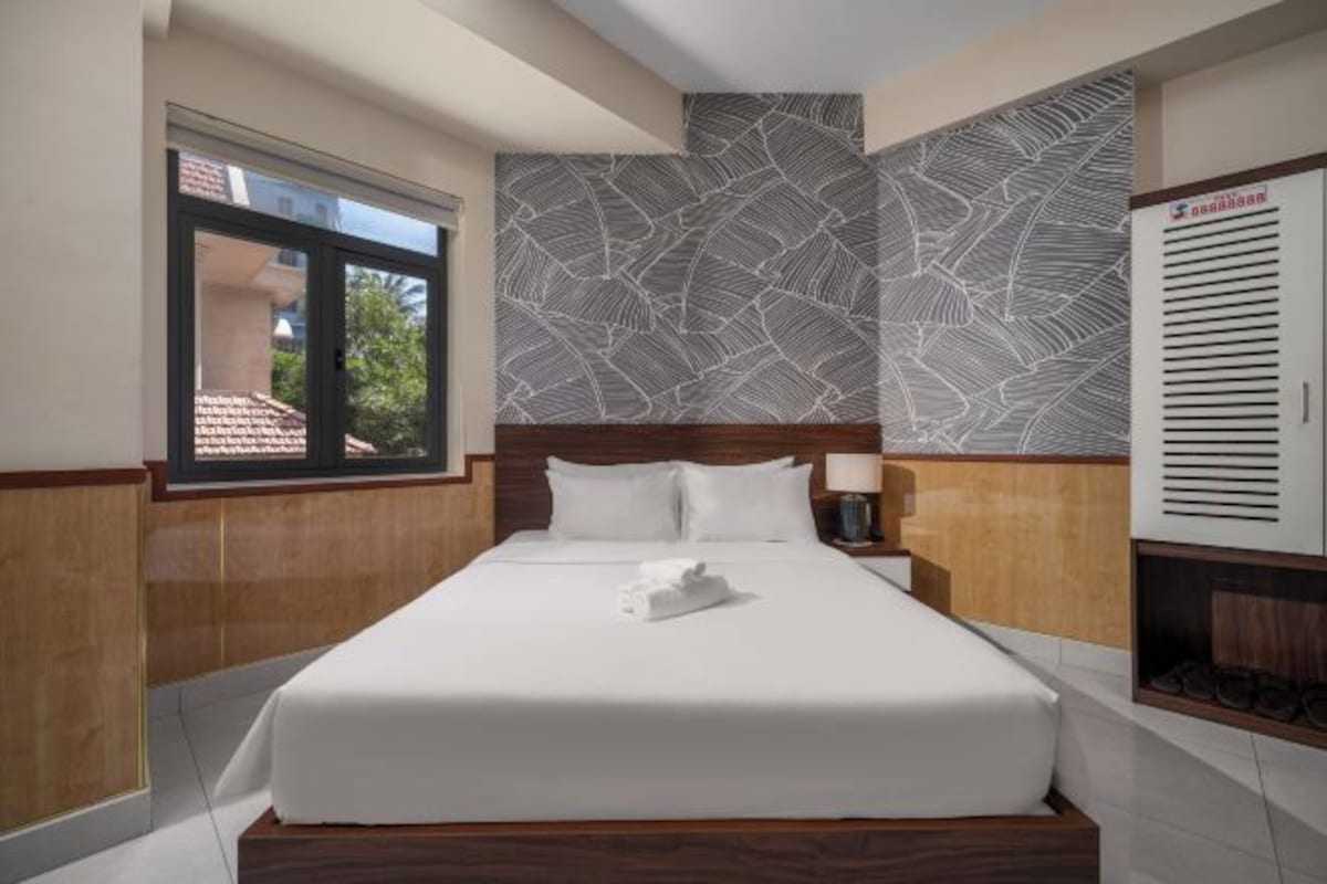 Ein Hotelzimmer mit einem großen Bett, einem Fenster, einer Wand mit Muster und einem Kleiderschrank.