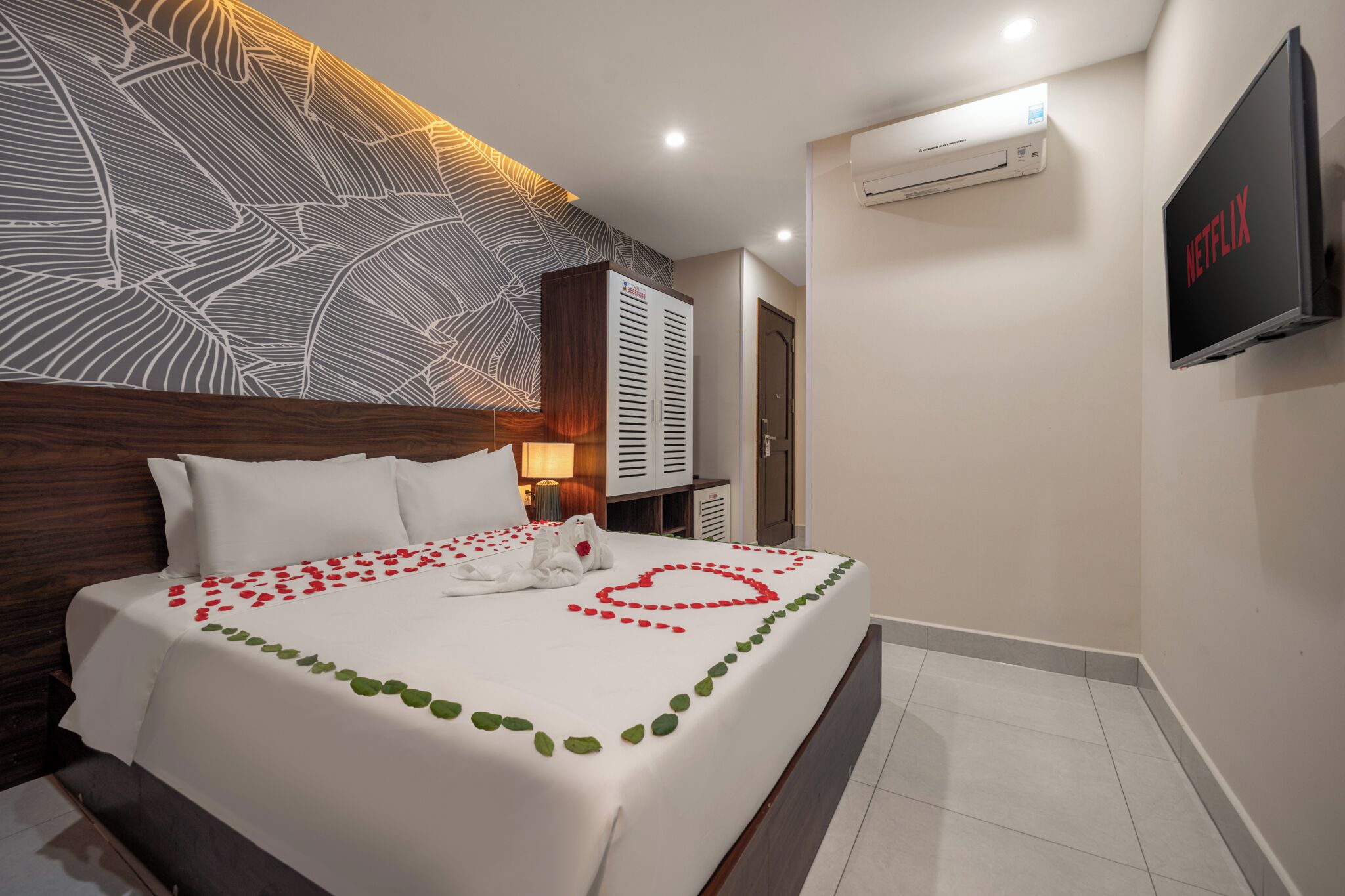 Ein Hotelzimmer mit einem ordentlich bezogenen Bett, einem an der Wand montierten Fernseher und einer Klimaanlage.