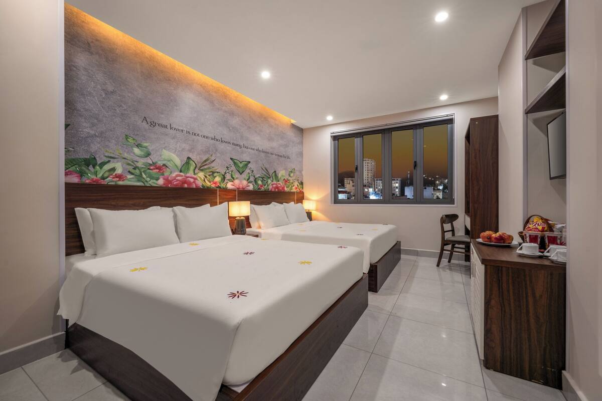 A hotel room with two beds, a desk with a chair, a large window, and a city view.