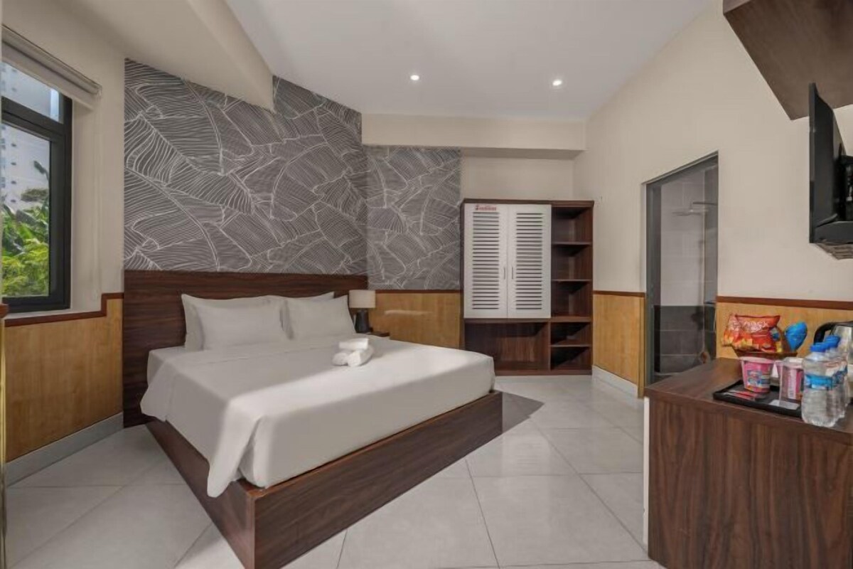 Une chambre d’hôtel moderne dotée d’un grand lit, d’une armoire, d’un bureau avec des articles de toilette et d’un téléviseur fixé au mur.