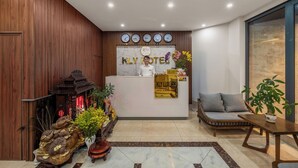 A hotel reception area with a wooden reception desk, a sofa, and a plant. - KLY Hotel Vung Tau (Ho Chi Minh City)