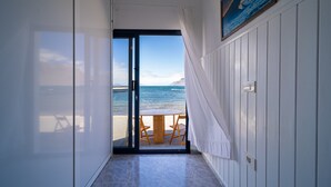 A corridor leading to a balcony with a view of the sea, a wooden table, and chairs.