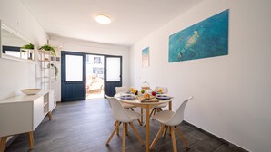 A modern dining area with a round table, white chairs, and a view through a glass door to an outdoor space.