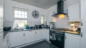A kitchen with white cabinets, a black stove, a clock on the wall, and a window with a view. - Cosy & Central 2Bd Apartment Milngavie, Glasgow (Glasgow)