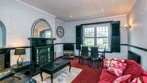 A living room with a fireplace, a television, a sofa, and a dining area with chairs. - Cosy & Central 2Bd Apartment Milngavie, Glasgow (Glasgow)