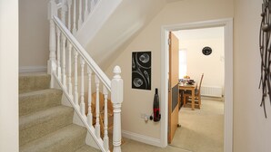 A carpeted staircase with white balusters, a dining area with a table and chairs, and a clock on the wall.