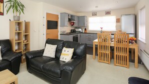 A compact living space with a black leather sofa, wooden dining table, and kitchen area including a microwave and refrigerator.