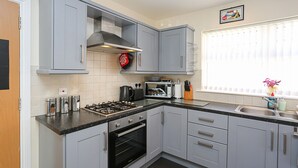 A kitchen with grey cabinets, a stove, oven, microwave, and a window with blinds.