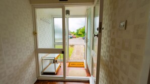 A hallway with a wooden floor, a glass door leading outside, and a welcome mat at the entrance.