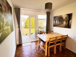 A dining area with a wooden table and chairs, a large window with curtains, and a painting on the wall.