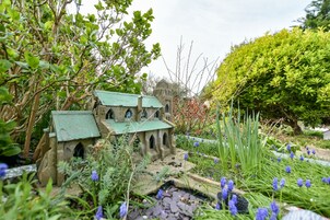 A miniature model of a house surrounded by greenery and flowers.