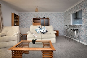A living room with a sofa, a wooden coffee table, a cabinet, and a bar stool. - Amazing Beachside 2Bd Family Home With Garden (Margate)