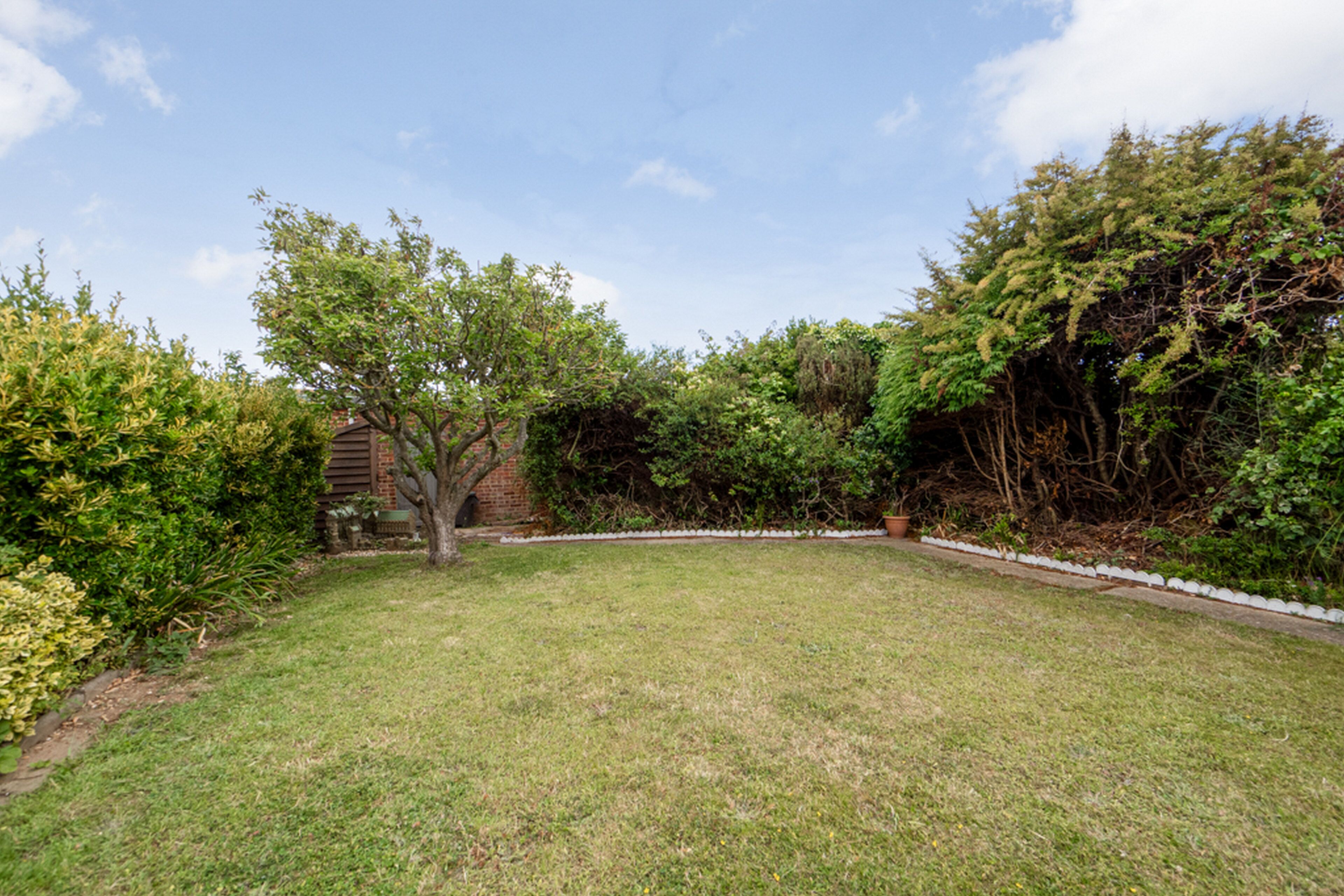 A well-maintained grassy backyard with mature trees, a brick structure, and a white border.