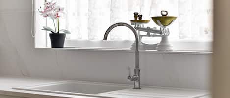 A kitchen with a white sink, a faucet, and a window with sheer curtains.