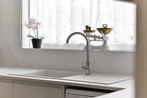 Una cocina con un lavamanos blanco, un grifo y una ventana con cortinas traslúcidas.