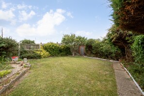 A grassy backyard with a brick structure, a wooden fence, and dense shrubbery. - Amazing Beachside 2Bd Family Home With Garden (Margate)