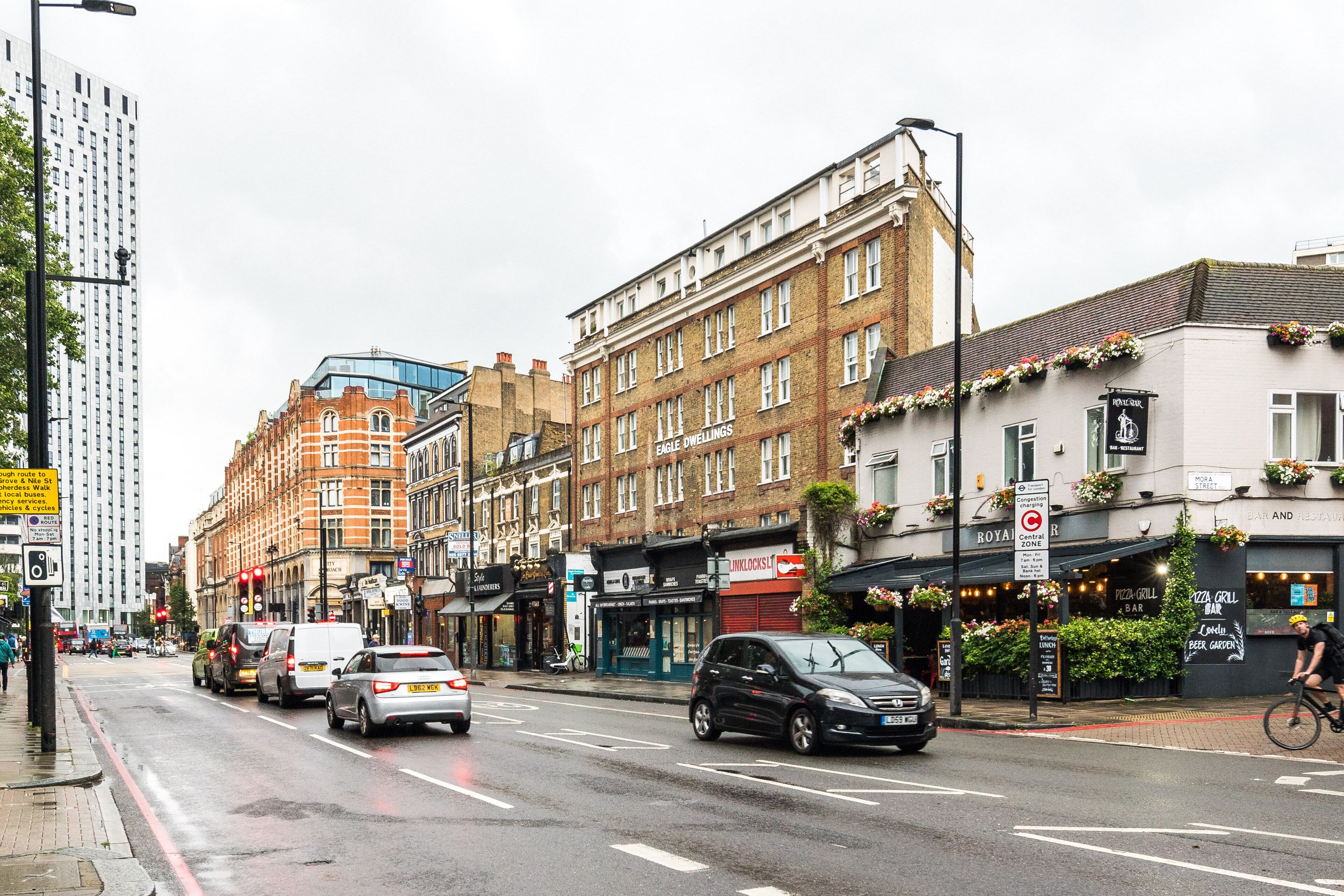 A street with buildings, including a pub with outdoor seating and a sign for 'Pizza Grill Bar'.