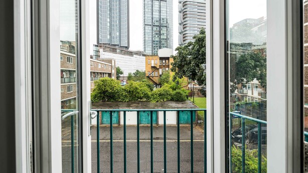 Une vue depuis une fenêtre donnant sur un paysage urbain, avec de hauts immeubles, une clôture verte et un vélo garé.