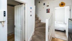 Un escalier menant à une chambre à coucher, où se trouvent un lit, une porte blanche et un mur orné de tableaux.