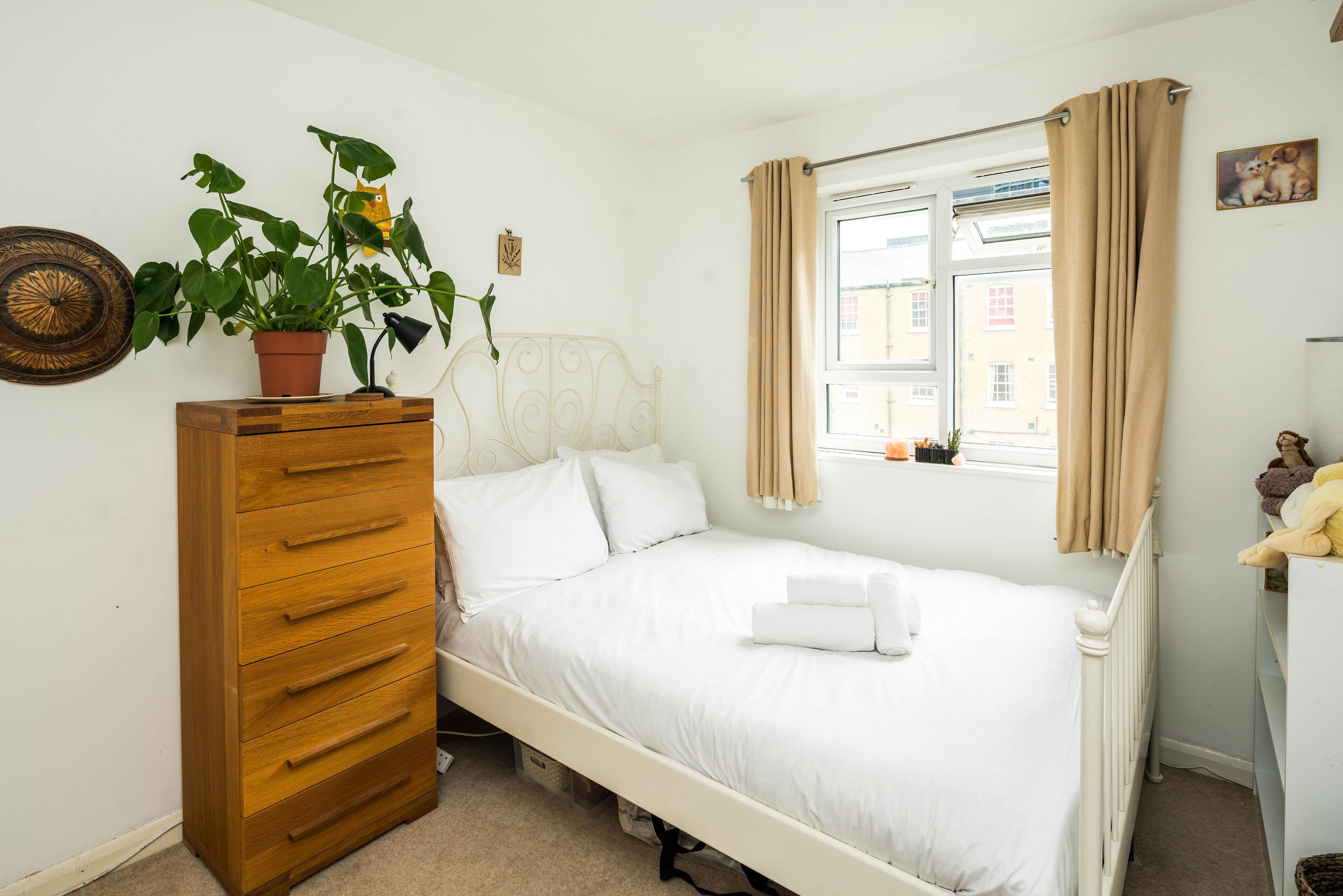Quarto com uma cama de solteiro, cômoda de madeira, planta em vaso, janela com cortinas e radiador.