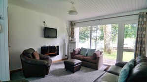 A living room with leather sofas, a flat-screen TV, and a fireplace. - Special 2 Bedroom Home In White Cross (Newquay)