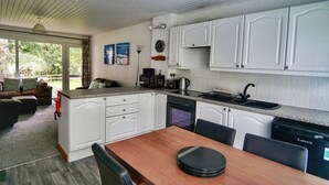 A modern kitchen with white cabinets, a wooden dining table, and a view of the outdoors. - Special 2 Bedroom Home In White Cross (Newquay)