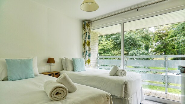 A bedroom with two beds, each with a rolled towel, white bedding, and a view of a green landscape through a large window. - Special 2 Bedroom Home In White Cross (Newquay)