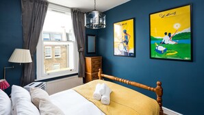 A bedroom with a bed, a window with curtains, a lamp, a dresser, and two framed pictures on the wall.