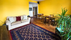 A living room with a sofa, a dining table, chairs, a patterned rug, and a potted plant.