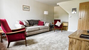 Un salon avec un canapé, un fauteuil rouge, un meuble en bois et une lampe.