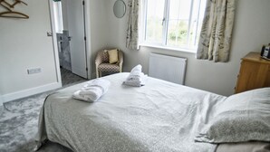 Une chambre d’hôtel avec un lit, une chaise, un radiateur et une fenêtre avec des rideaux.
