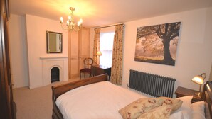 A bedroom with a bed, a chair, a fireplace, a radiator, a lamp, and a painting of a tree. - Delightful Cottage In Sandwich - One Bedroom (Sandwich)