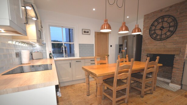 A modern kitchen with wooden flooring, a dining table with chairs, pendant lights, and a brick fireplace. - Delightful Cottage In Sandwich - One Bedroom (Sandwich)